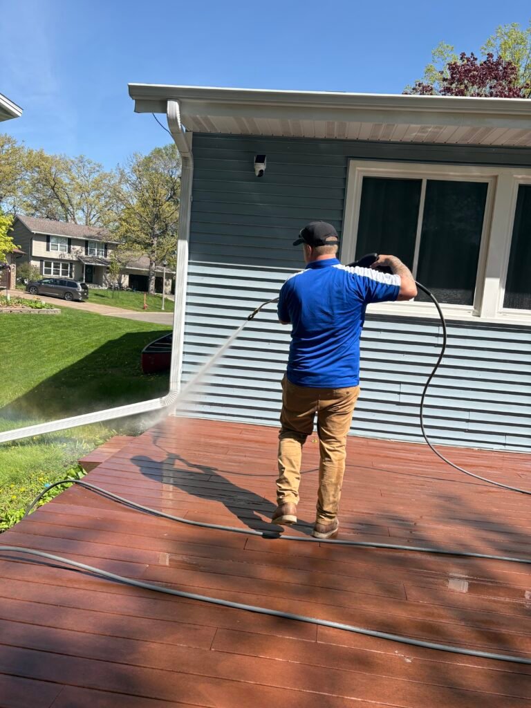 man in blue shirt and tan pants spraying a brick patio