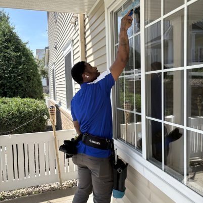 man in blue shirt in front of a home cleaning the exterior side of large windows