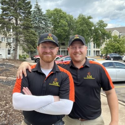 two guys standing on a sidewalk both wearing black hats and black with red shirts with the S&M Cleaning Solutions logo