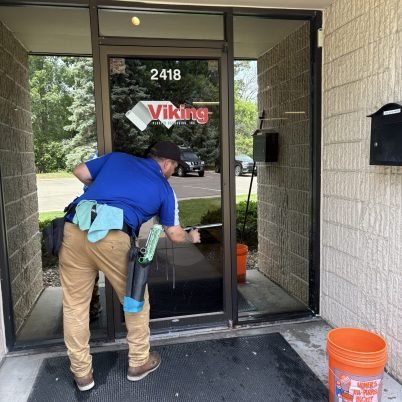 man in blue shirt, tan pants, cleaning a glass door