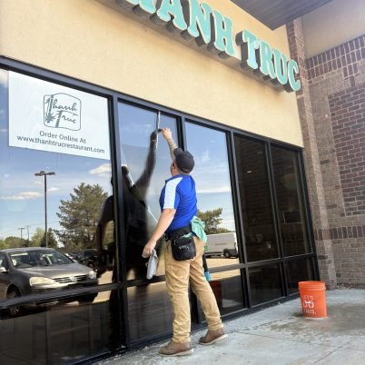 man in front of business in a blue shirt and black tool belt cleaning the big windows