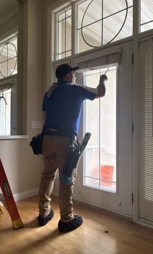 man in blue shirt next to a ladder cleaning the interior side of windows and glass door