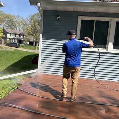 man in blue shirt and tan pants spraying a brick patio