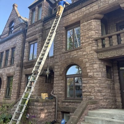 man at the top of a very tall ladder leaned onto a tall brick castle like home to clean the cutters
