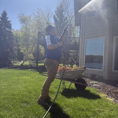 man in grass spraying the side of a home