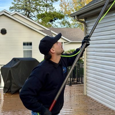 man in dark hoodie and dark hat with a long pole cleaning windows