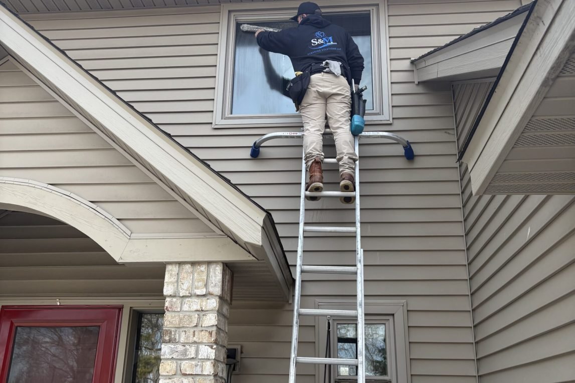 man on high ladder cleaning windows